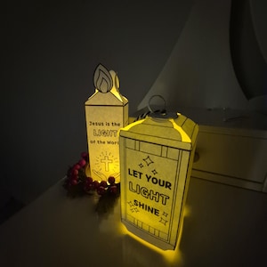 May include: Two illuminated paper lanterns with religious text. One lantern reads "Jesus is the LIGHT of the World" with a cross graphic. The other lantern says "LET YOUR LIGHT SHINE". Both are lit from within, creating a warm glow.