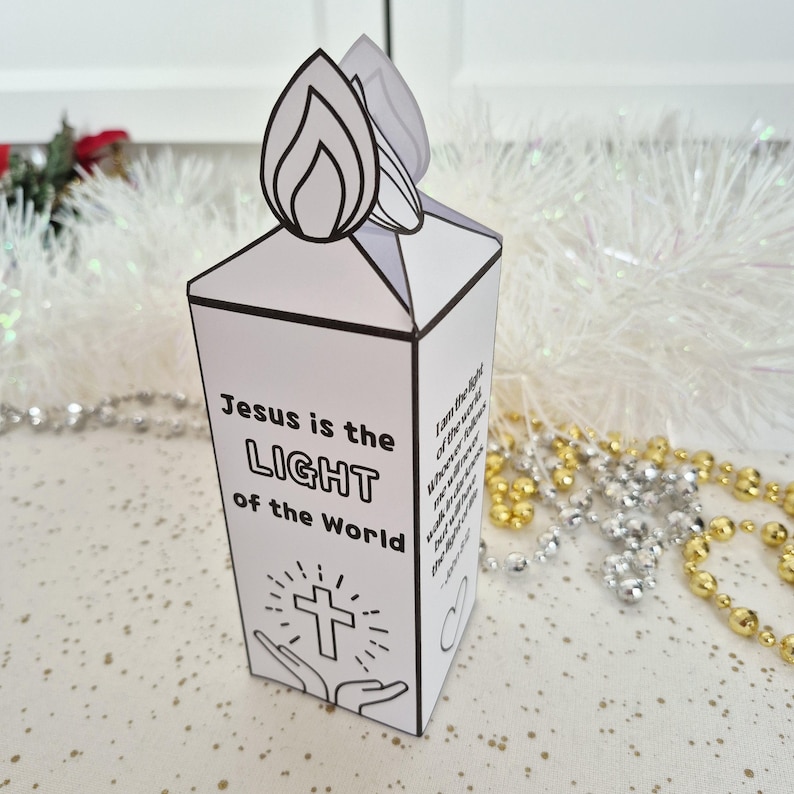 May include: A white paper candle-shaped box with the text "Jesus is the LIGHT of the World" and a cross graphic. The top features a flame design. Religious-themed craft.