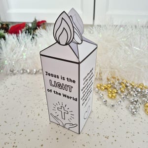 May include: A white paper candle-shaped decoration with a flame design on top. The text "Jesus is the LIGHT of the World" is printed on the front, along with a cross and hands. Additional text is on the side.