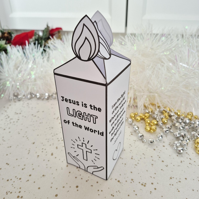 May include: A white paper candle-shaped decoration with a flame design on top. The text "Jesus is the LIGHT of the World" is printed on the front, along with a cross and hands. Additional text is on the side.