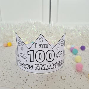May include: A white paper crown with the text "I am 100 Days Smarter" in black. The crown has star and heart designs, and is decorated with colorful pom-poms. Perfect for a child's milestone celebration.