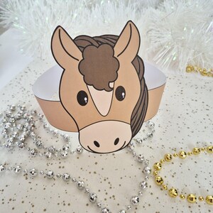 Pu&ograve; includere: Una corona di cavallo di carta con un viso marrone chiaro, una criniera marrone scuro e una fascia bianca. Il cavallo ha grandi occhi neri e un muso marrone chiaro. Sullo sfondo ci sono perline decorative argentate e dorate.