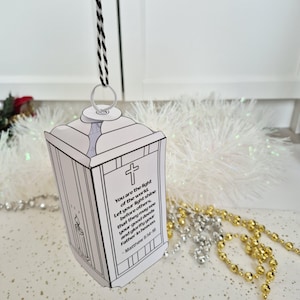 May include: A white paper lantern with a black and white cord for hanging. The lantern has a cross and text from Matthew 5:14-16. The lantern is a religious-themed craft.