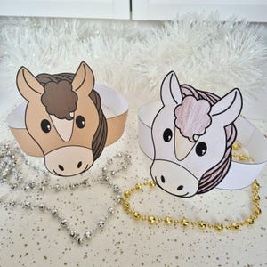 Pu&ograve; includere: Due corone di carta a tema cavallo. Una corona presenta un cavallo marrone con una criniera marrone, mentre l'altra ha un cavallo bianco con una criniera rosa. Entrambe le corone hanno una fascia bianca. Collane di perline argentate e dorate in primo piano.
