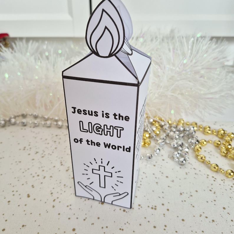 May include: A white paper candle with a flame-shaped top. The candle features the text "Jesus is the LIGHT of the World" with a cross and hands illustration. Decorative beads are in the background.