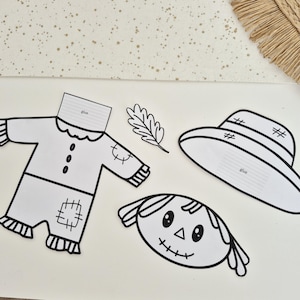 May include: A black and white paper craft set featuring a scarecrow outfit, a hat, a leaf, and a face. The clothing and hat pieces include a tab labeled glue for assembly. The scarecrow face has stitched eyes, a triangular nose, and a stitched mouth.