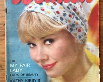 May include: A vintage magazine cover featuring a woman with blonde hair wearing a floral headband. The magazine is titled "Woman" and the text "The My Fair Lady Look of Beauty" is visible. The magazine cover is from April 17, 1965.