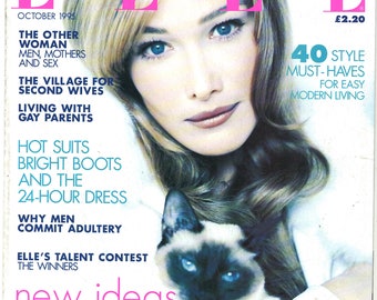 Può includere: Una copertina di rivista con una donna dai capelli biondi e occhi azzurri, vestita con una camicia bianca e che tiene un gatto siamese. La rivista si chiama "ELLE" e il testo della copertina recita "new ideas natural beauty" e "Winter Hair and Skincare Special Plus the Best Looks from the Catwalk".