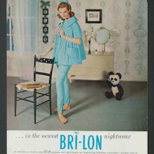 Op de afbeelding: Een vrouw in een lichtblauwe pyjamaset staat in een slaapkamer. Ze houdt een witte bloem vast. De tekst "BRI-LON nightwear" is in grote letters onderaan de afbeelding gedrukt. De tekst "As colourful as they're cosy, BRI-LON pyjamas and nightdresses are brightening bedrooms everywhere! Autumn Pink or Autumn Blue - pick your fashion colour in your favourite style and you'll be Miss Sleeping Beauty 1960! Remember, too, that BRI-LON nightwear washes in a moment and drip-dries perfectly as only nylon can. So civilised! See it." is onder de grote tekst gedrukt.