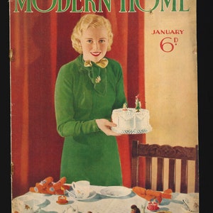Puede incluir: Una mujer con un vestido verde sostiene un pastel blanco decorado con pequeños árboles verdes y glaseado blanco. El pastel está en un plato blanco. La mujer está de pie frente a una cortina roja. La portada de la revista dice "MODERN HOME" y "JANUARY 6d." El texto en la parte inferior de la portada dice "HAPPY IDEAS for Your NEW YEAR PARTIES."