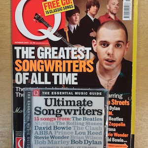 Puede incluir: Una revista musical, "The Essential Music Guide", con una portada que presenta una banda y el titular "The Greatest Songwriters of All Time". Una caja de CD con "Ultimate Songwriters" está frente a la revista.