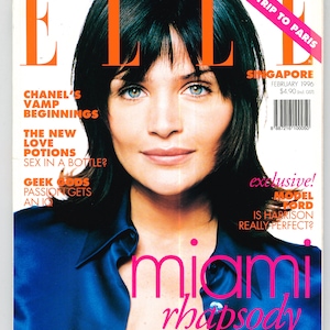 May include: A magazine cover featuring a woman with dark hair and blue eyes wearing a blue shirt. The magazine is titled "ELLE" and the cover text reads "Miami Rhapsody, Bikinis to Dive For".