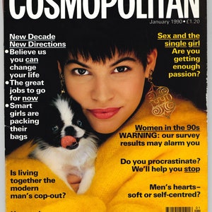 Può includere: Copertina della rivista Cosmopolitan del gennaio 1990. La copertina presenta una donna con capelli scuri corti e orecchini d'oro, che tiene in braccio un piccolo cane bianco e nero. Il titolo della rivista è in grandi lettere bianche.
