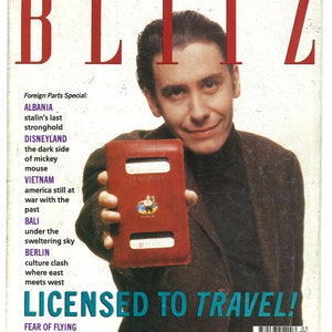 Könnte beinhalten: Ein Magazincover mit dem Titel "BLITZ" in roten Buchstaben. Das Cover zeigt einen Mann, der einen roten Reisepass hält. Der Text "LICENSED TO TRAVEL!" ist in blauen Buchstaben. Das Magazin ist aus dem März 1990.
