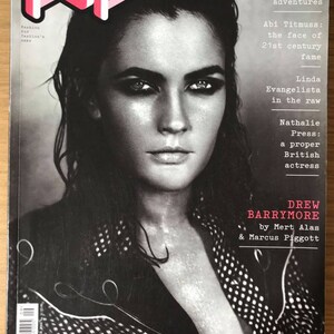 Pode incluir: Uma capa de revista em preto e branco com Drew Barrymore com o título "Drew Barrymore" e o texto "by Mert Alas & Marcus Piggott".
