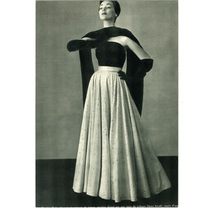 May include: A black strapless gown with a white skirt covered in sequins. The gown has a black velvet sash and is paired with black gloves.