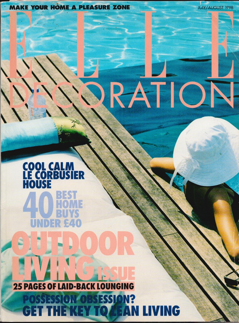 May include: A magazine cover featuring a woman in a white sun hat relaxing by a pool. The magazine is titled "ELLE Decoration" and the cover story is "Outdoor Living Issue". The cover also features the text "Cool Calm Le Corbusier House" and "40 Best Home Buys Under $40".