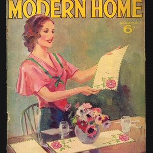 May include: Vintage magazine cover for Modern Home, March 1933, featuring a woman holding a floral-decorated placemat. The cover advertises "Free Gift Transfers Inside." A table is set with matching placemats, flowers, and glassware. The text reads "Set for Two."