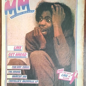 Op de afbeelding: Een tijdschriftcover met een zwart-witfoto van een man met een bezorgde uitdrukking. Het tijdschrift heet "Melody Maker" en bevat de tekst "Linx Get Ahead" in een rode box. De cover bevat ook de tekst "Fun Boy Three, The Sound, Haircut 100, Costello's Nashville LP".