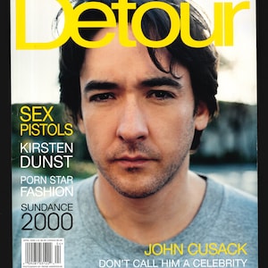 Op de afbeelding: Een tijdschriftcover met John Cusack, met de titel "Detour" in gele letters. De cover bevat ook de tekst "Sex Pistols", "Kirsten Dunst", "Porn Star Fashion", "Sundance 2000" en "Don't Call Him a Celebrity".