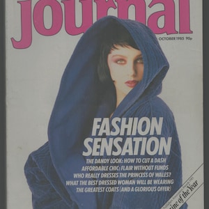 May include: A magazine cover featuring a woman wearing a blue hooded jacket. The magazine is titled "woman's journal" and the cover text reads "Fashion Sensation". The magazine cover also includes the text "The Dandy Look: How to Cut a Dash, Affordable Chic: Flair Without Funds, Who Really Dresses the Princess of Wales? What the Best Dressed Woman Will Be Wearing, The Greatest Coats (And a Glorious Offer)".