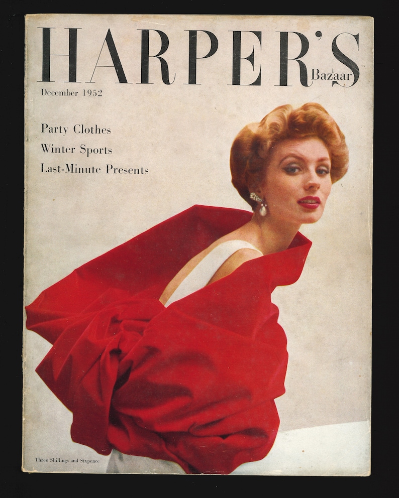 Op de afbeelding: Een vintage magazinecover voor Harper's Bazaar, december 1952, met een vrouw in een witte jurk en een rode cape. De tekst op de cover luidt "Party Clothes, Winter Sports, Last-Minute Presents".