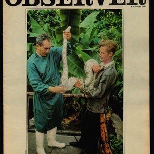 May include: A black and white magazine cover with the title "OBSERVER" in bold, white letters. The date "6 AUGUST 1967" is printed in the top right corner. The cover features a photo of two men in a tropical setting, one holding a large python snake. The caption below the photo reads "HOW DO YOU CURE A PYTHON OF A PAIN IN THE BELLY?"