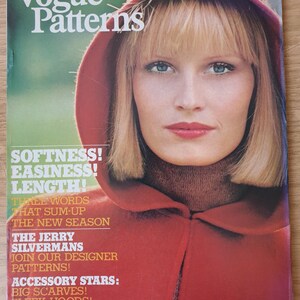 May include: A vintage Vogue Patterns magazine cover featuring a woman wearing a red hooded sweater. The cover text reads "Softness! Easiness! Length!" and "The Jerry Silvermans Join Our Designer Patterns!"  The magazine is from Autumn 1974.