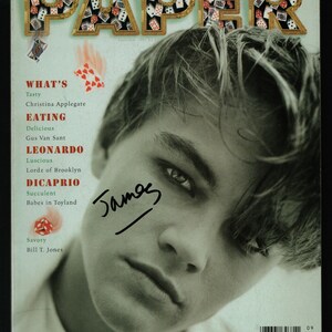 Pode incluir: Uma capa de revista com um retrato de perto de Leonardo DiCaprio. A revista é intitulada "PAPER" com as letras feitas de cartas de jogo. O texto "WHAT'S" está em vermelho e o texto "LEONARDO DICAPRIO" está em preto. A capa também inclui o texto "James" em itálico preto.