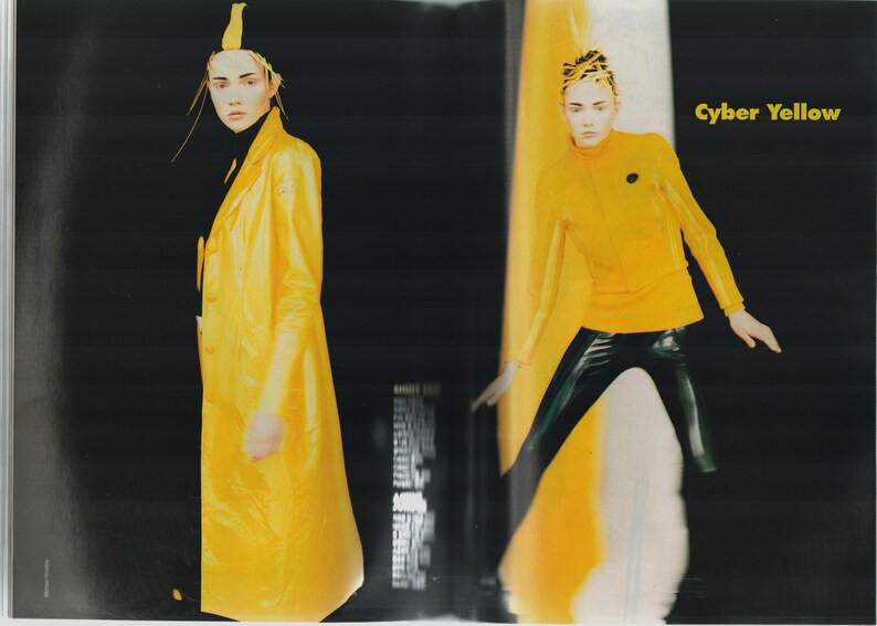 May include: Two women wearing yellow clothing. The woman on the left is wearing a long yellow coat and a black turtleneck. The woman on the right is wearing a yellow turtleneck and black pants. The text "Cyber Yellow" is printed in black on a yellow background.