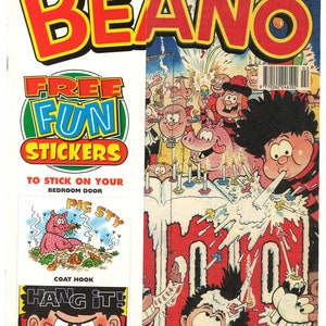 Op de afbeelding: Een vintage comicboekomslag met de Beano-mascotte, Dennis de Menace, met de tekst "The Beano" in rode en gele letters. De omslag toont Dennis met een verjaardagstaart en andere personages uit de comic. De tekst "Free Fun Stickers" staat aan de linkerkant van de omslag.