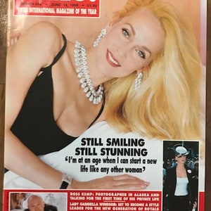 May include: A magazine cover featuring Jerry Hall, a model and actress, with the title "HELLO!" and the text "Still Smiling Still Stunning." The cover also features a smaller image of a woman in a white shirt and black skirt.