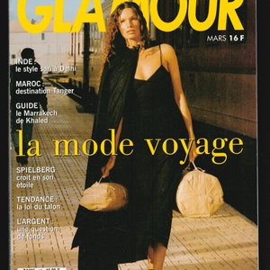 May include: A magazine cover featuring a woman in a black dress and sandals, holding two wrapped packages. The magazine is titled "Glamour" and the cover text reads "la mode voyage".