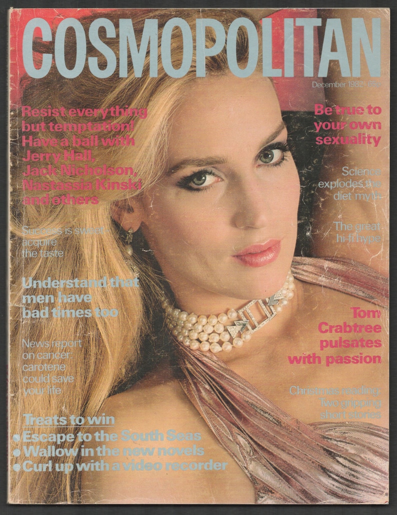 以下が含まれることがあります： 1982年12月号のCosmopolitan誌の表紙。ブロンドの髪の女性が、真珠のネックレスとピンクのドレスを着ています。雑誌のタイトルは薄い青色の文字で表示されています。