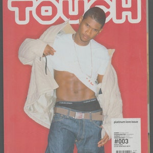 May include: A magazine cover featuring a man wearing a white t-shirt, jeans, and a black belt. The magazine is titled "Touch" and the cover features the text "platinum love issue" and "#003".