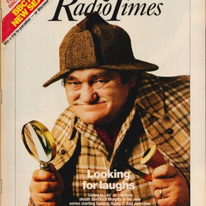 May include: A magazine cover featuring a man wearing a brown tweed hat and a plaid shirt. He is holding a magnifying glass in one hand and a pipe in the other. The magazine cover is for Radio Times and the headline is "Looking for laughs".