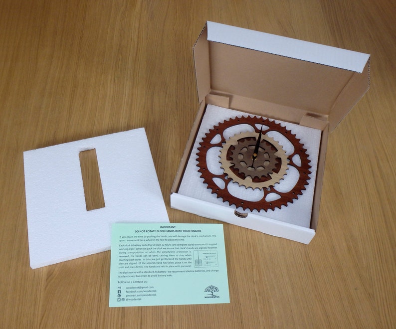 Pode incluir: Um rel&oacute;gio de madeira com design de engrenagem, embalado em uma caixa branca com um inserto de espuma. O rel&oacute;gio tem duas engrenagens, uma marrom e outra de madeira natural. Os ponteiros do rel&oacute;gio s&atilde;o pretos. A caixa inclui um cart&atilde;o de instru&ccedil;&otilde;es verde e branco com o texto "N&Atilde;O GIRE AS AGULHAS DO REL&Oacute;GIO COM OS DEDOS".