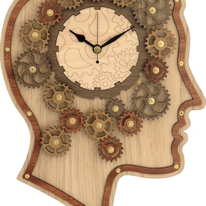 Op de afbeelding: Een houten wandklok in de vorm van een mensenhoofd met tandwielen en een wijzerplaat in het midden. De wijzerplaat heeft een lichte houten achtergrond met een donker houten patroon en zwarte wijzers.