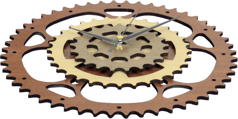 Pode incluir: Um rel&oacute;gio de parede de madeira com um anel exterior castanho e um anel interior dourado. O mostrador do rel&oacute;gio &eacute; composto por tr&ecirc;s engrenagens interligadas. Os ponteiros do rel&oacute;gio s&atilde;o pretos.