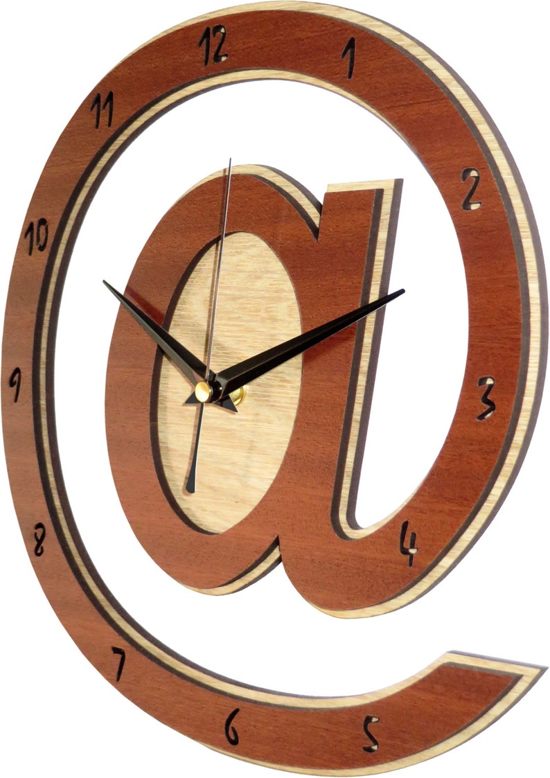 May include: A wooden wall clock with a brown and natural wood finish. The clock face is shaped like the "@" symbol. The clock hands are black and the numbers are black on a white background.