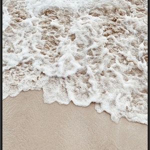 May include: Close-up of foamy white ocean waves crashing on a sandy beach. The sand is a light beige color.