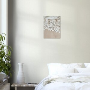 May include: Close-up of foamy white ocean waves crashing on a sandy beach. The sand is a light beige color.