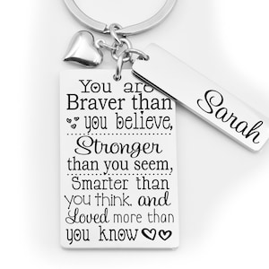 May include: Silver keychain with a heart charm and a rectangular tag that reads "You are Braver than you believe, Stronger than you seem, Smarter than you think, and Loved more than you know♡♡". A smaller rectangular tag with the name "Sarah" hangs from the keychain.