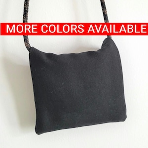 May include: A small black crossbody bag with a rope strap. The bag is made of a soft, textured fabric.  "MORE COLORS AVAILABLE" is written in red letters across the top of the image.
