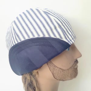 May include: A cap featuring a white and navy blue pinstriped pattern on the upper section and a solid navy blue band along the lower edge. The headwear has a rounded crown and a structured design that fits snugly around the head, showcasing a contrast.