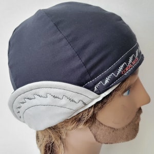 May include: A black and white cycling cap with a white brim and a black crown. The cap has a white zig-zag pattern around the brim and the text "CORAL 100" in red on the side.