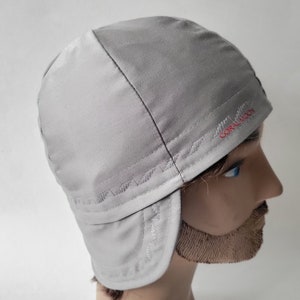 Pu&ograve; includere: Un cappello grigio con paraorecchie, foderato in pile, con un logo ricamato in rosso che dice "CORAL MOON".