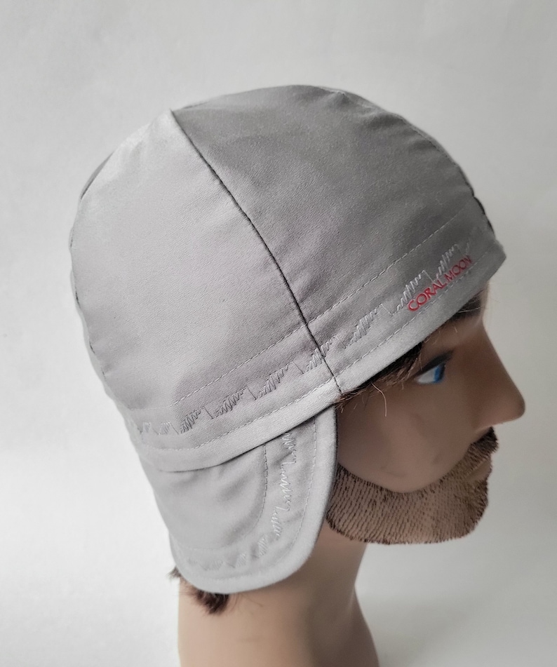 Pu&ograve; includere: Un cappello grigio con paraorecchie, foderato in pile, con un logo ricamato in rosso che dice "CORAL MOON".