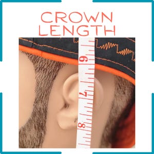 May include: A black cap with orange trim and a jagged orange line pattern, shown on a mannequin head next to a white measuring tape that indicates a crown length measurement between 6 and 8 inches, with the text CROWN LENGTH at the top.