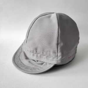 Pu&ograve; includere: Un berretto da ciclismo in cotone grigio con una visiera cucita e una piccola etichetta rossa con la scritta "CONVOY".